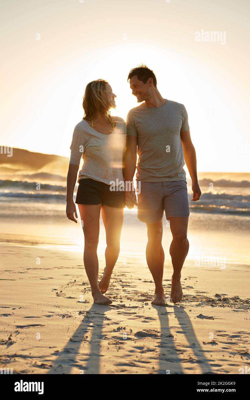 Ich bin so glücklich, dass ich mich auf ihn stützen kann. Aufnahme eines Paares, das bei Sonnenuntergang am Strand dicht beieinander läuft. Stockfoto