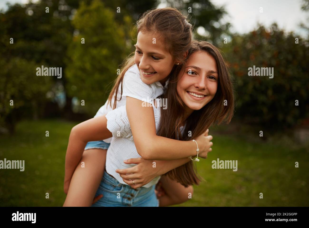 Ich bin ihr größter Unterstützer. Beschnittenes Porträt eines jungen Mädchens, das ihrer jüngeren Schwester eine Huckepack-Fahrt im Freien gab. Stockfoto