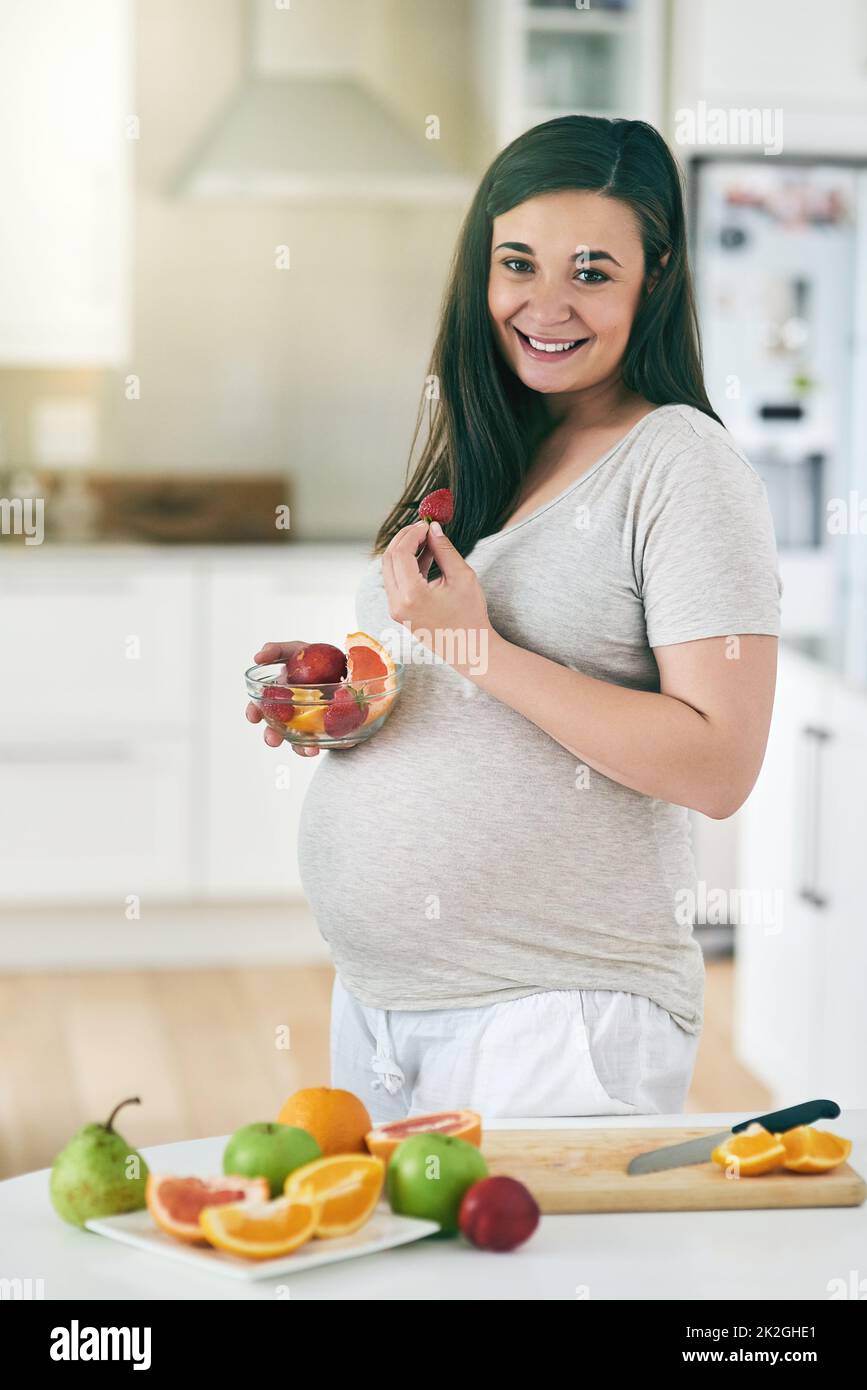 Gesunde Ernährung entspricht einem gesunden Baby. Aufnahme einer Schwangeren, die in ihrer Küche einen Obstsalat zubereitet. Stockfoto