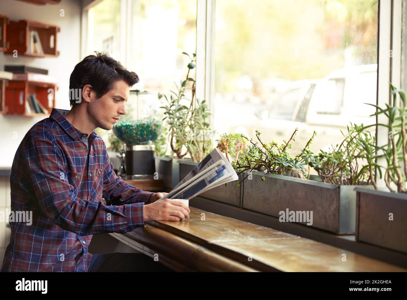 Aktualisierungen der alten Schule. Ausgeschnittene Aufnahme eines jungen Mannes, der in einem Café eine Zeitung liest. Stockfoto
