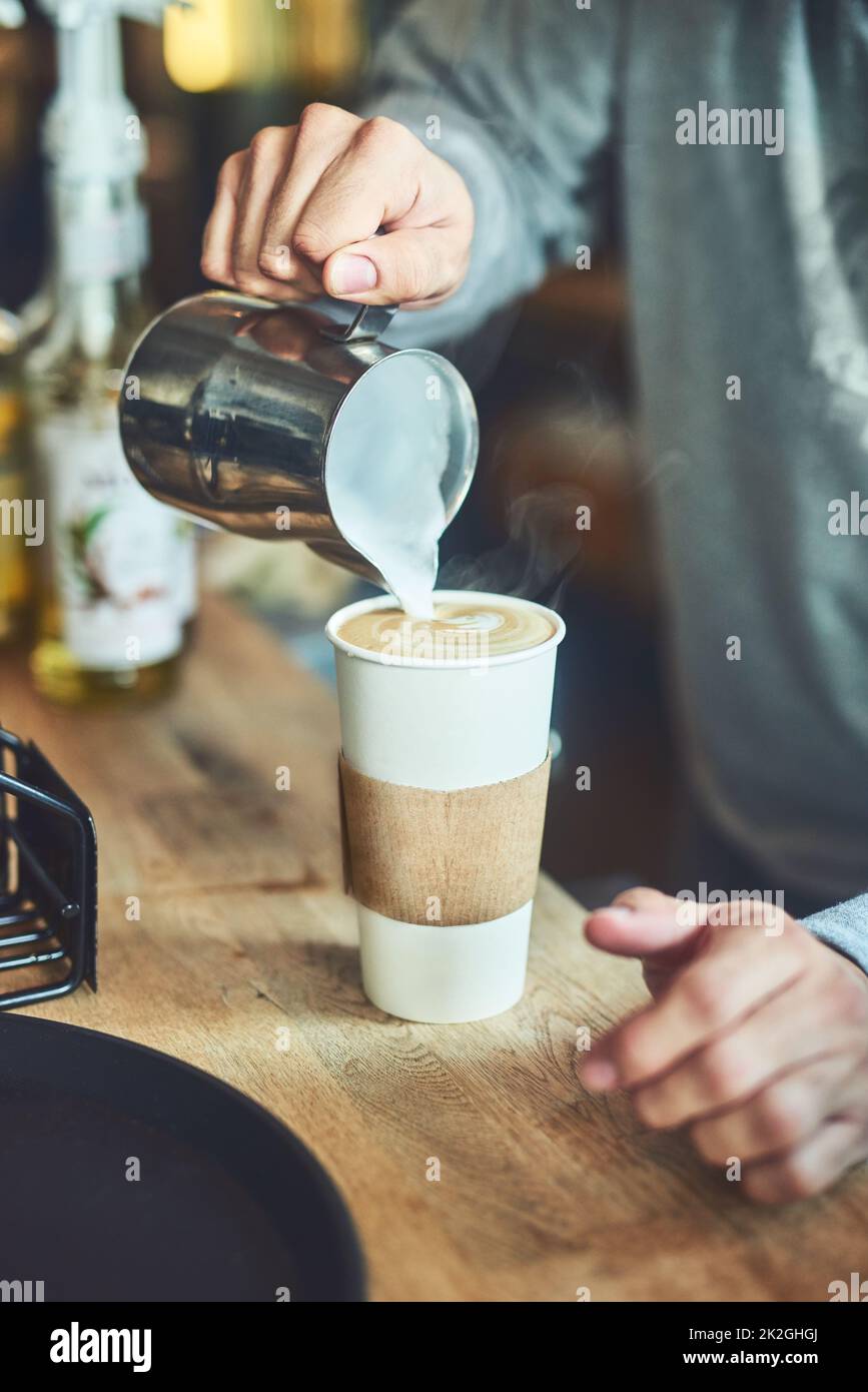 Mischen auf einer Tasse Magie. Nahaufnahme eines unerkennbaren Barista, der in einem Café Milch in eine Tasse frisch gebrühten Kaffee gießt. Stockfoto