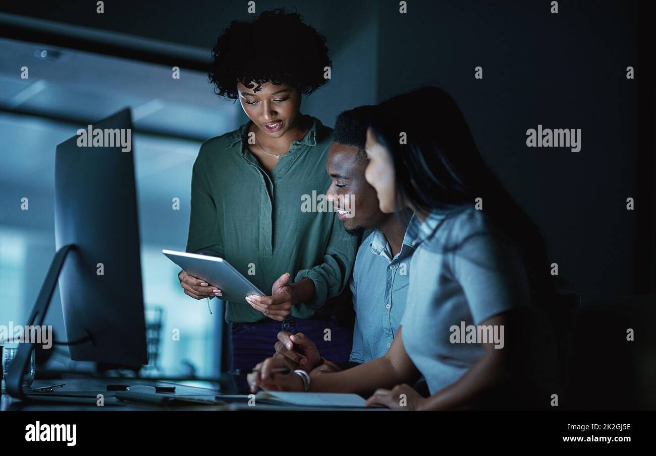 Der Kern des Erfolgs ist Engagement. Aufnahme einer Gruppe junger Geschäftsleute, die während einer späten Nacht auf der Arbeit ein digitales Tablet und einen Computer benutzten. Stockfoto