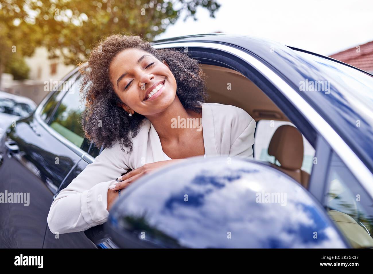 Den Wind in ihren Haaren spüren. Aufnahme einer attraktiven jungen Geschäftsfrau, die sich aus ihrem Fenster lehnte, während sie am Morgen zur Arbeit fuhr. Stockfoto