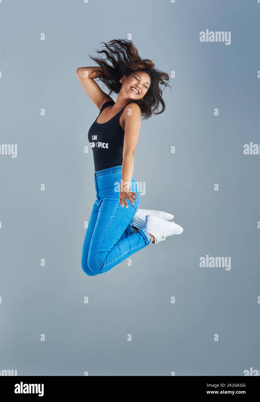 Springen vor Freude. Aufnahme einer attraktiven jungen Frau, die vor grauem Hintergrund posiert. Stockfoto