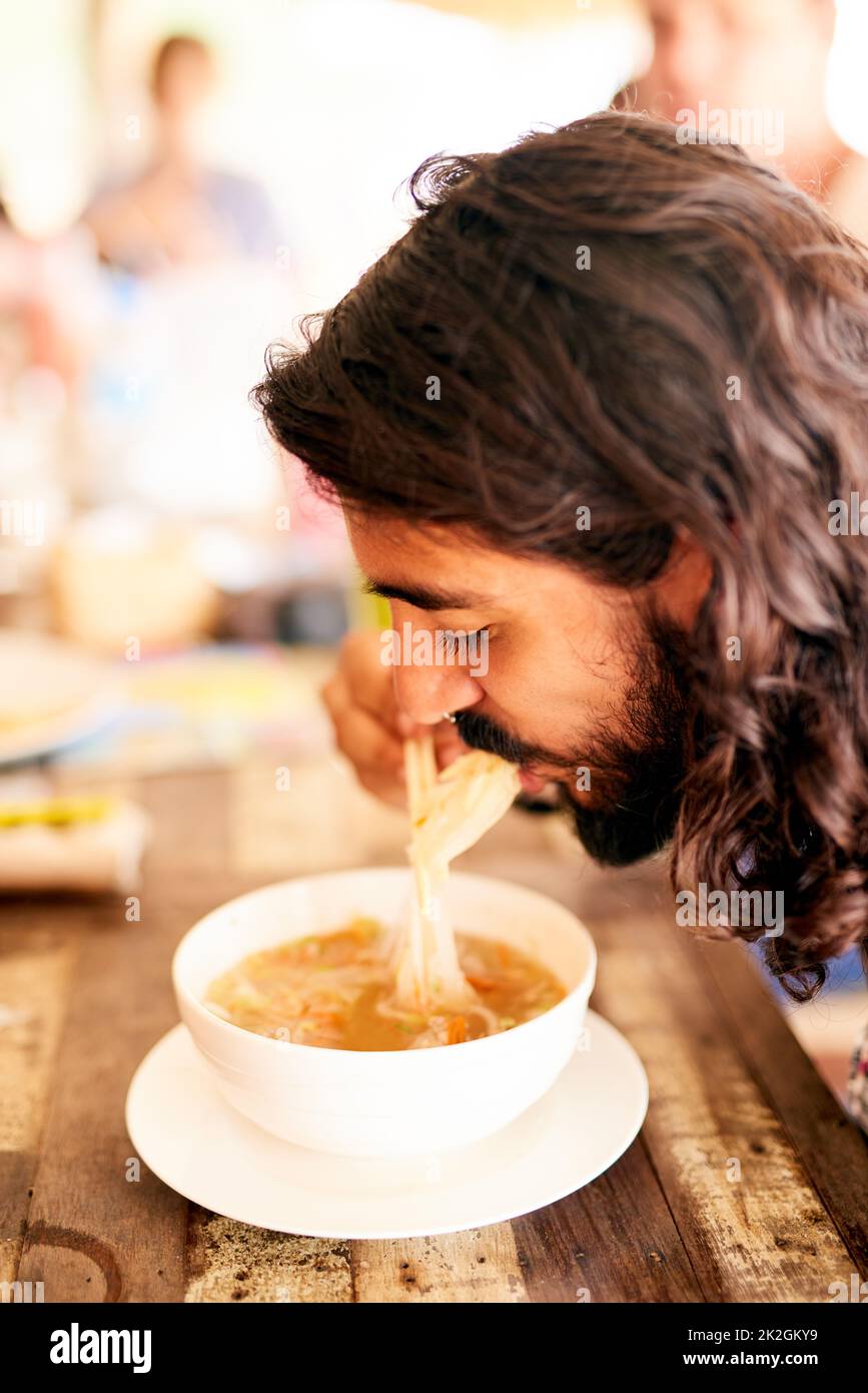 Genießen Sie eine Schüssel voller Nudeln. Aufnahme eines jungen Mannes, der in einem Restaurant in Thailand eine Schüssel mit Nudeln isst. Stockfoto