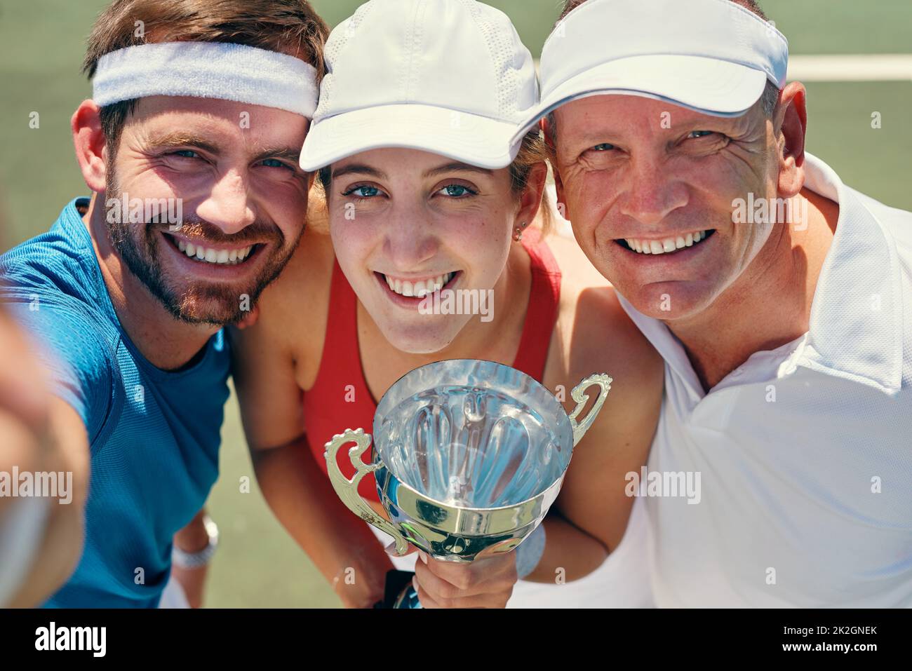 Ein großes Lächeln nach dem Sieg. Beschnittenes Porträt einer Gruppe von Sportlern, die nach dem Sieg eines Tennismatches zusammen stehen und eine Trophäe in der Hand halten. Stockfoto