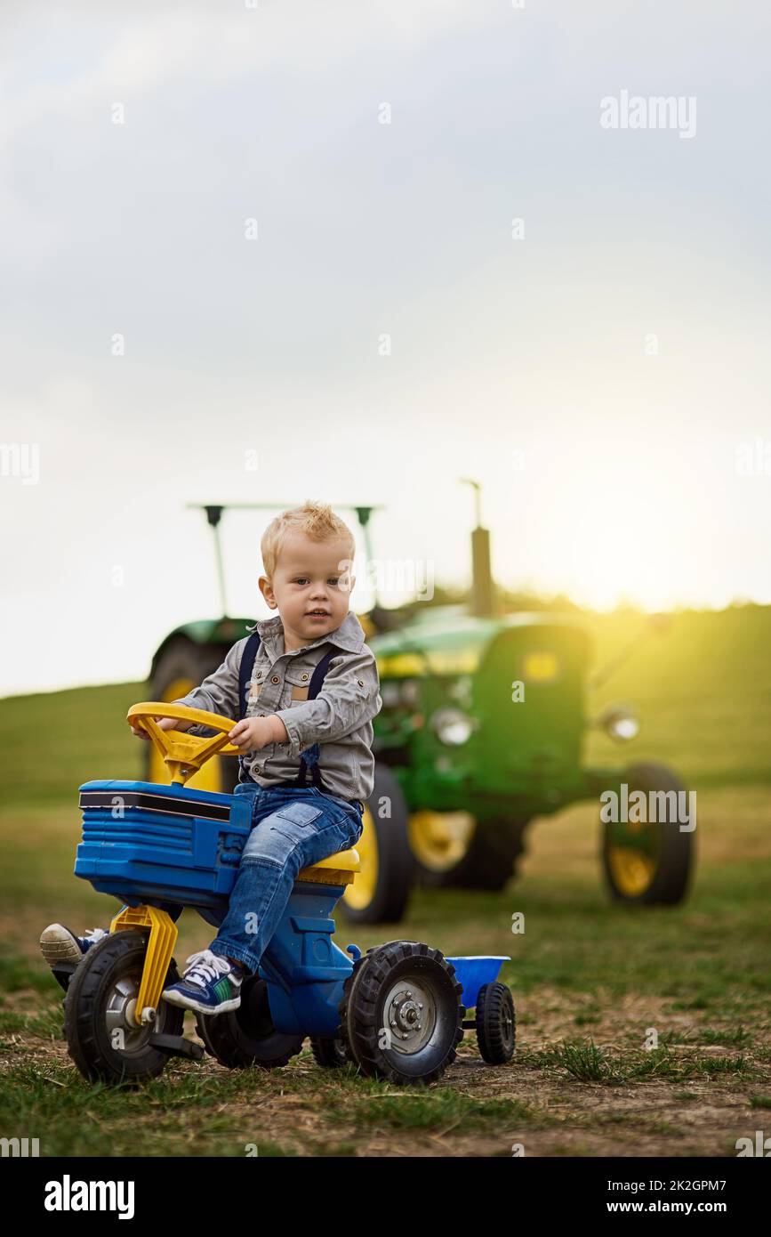 Es gibt wenig, was man nicht über das Leben auf dem Bauernhof lieben kann. Porträt eines entzückenden kleinen Jungen, der auf einem Spielzeugauto auf einer Farm reitet. Stockfoto