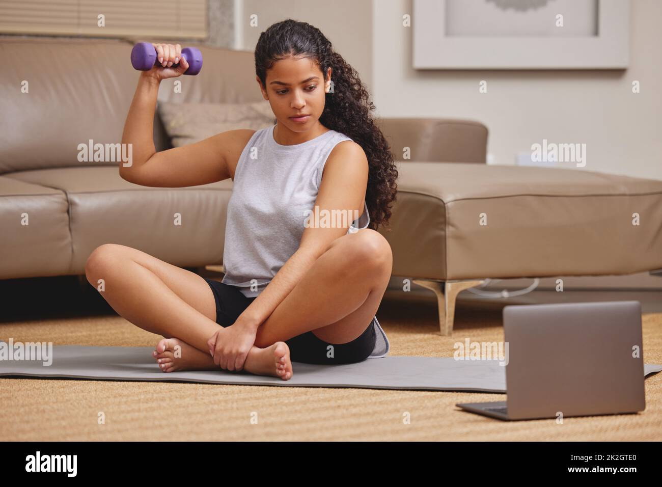 Heres zu stärkeren Armen. Ganzkörperaufnahme einer jungen Frau, die ihren Laptop benutzt, um einen Online-Fitnesskurs in ihrem Wohnzimmer zu verfolgen. Stockfoto