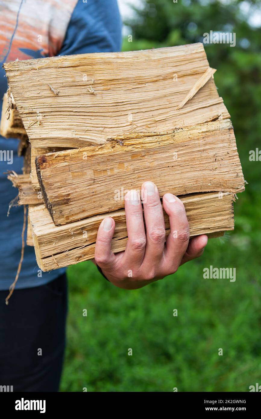 Die Hände des Mannes halten Feuerholz. Ein nicht erkennbarer Mann trägt Feuerholz zum Haus, um einen Kamin anzuzünden. Rustikale Landschaft Hintergrund. Stockfoto