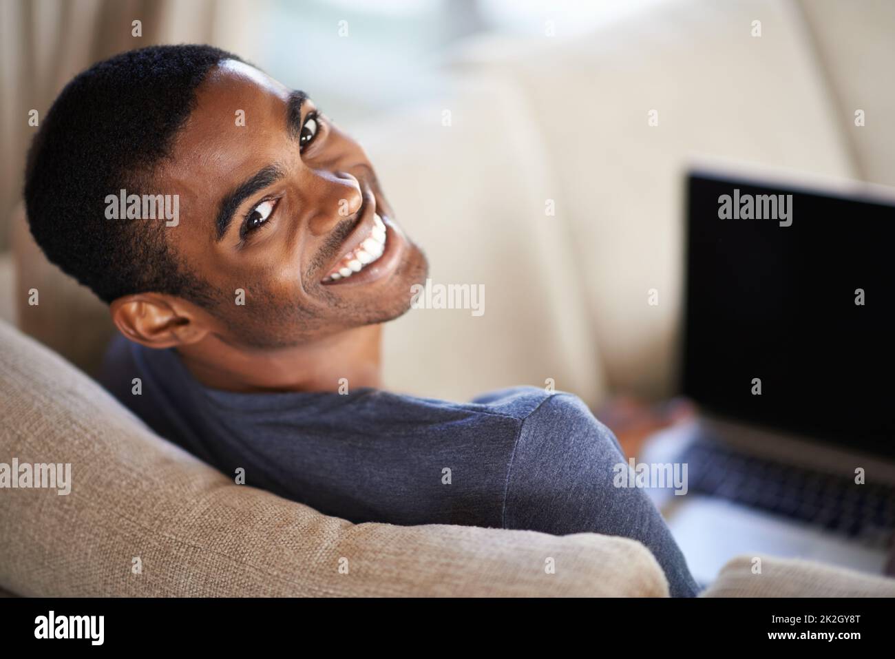 Ein schöner junger Mann, der seinen Laptop benutzt, während er sich zu Hause entspannt. Stockfoto