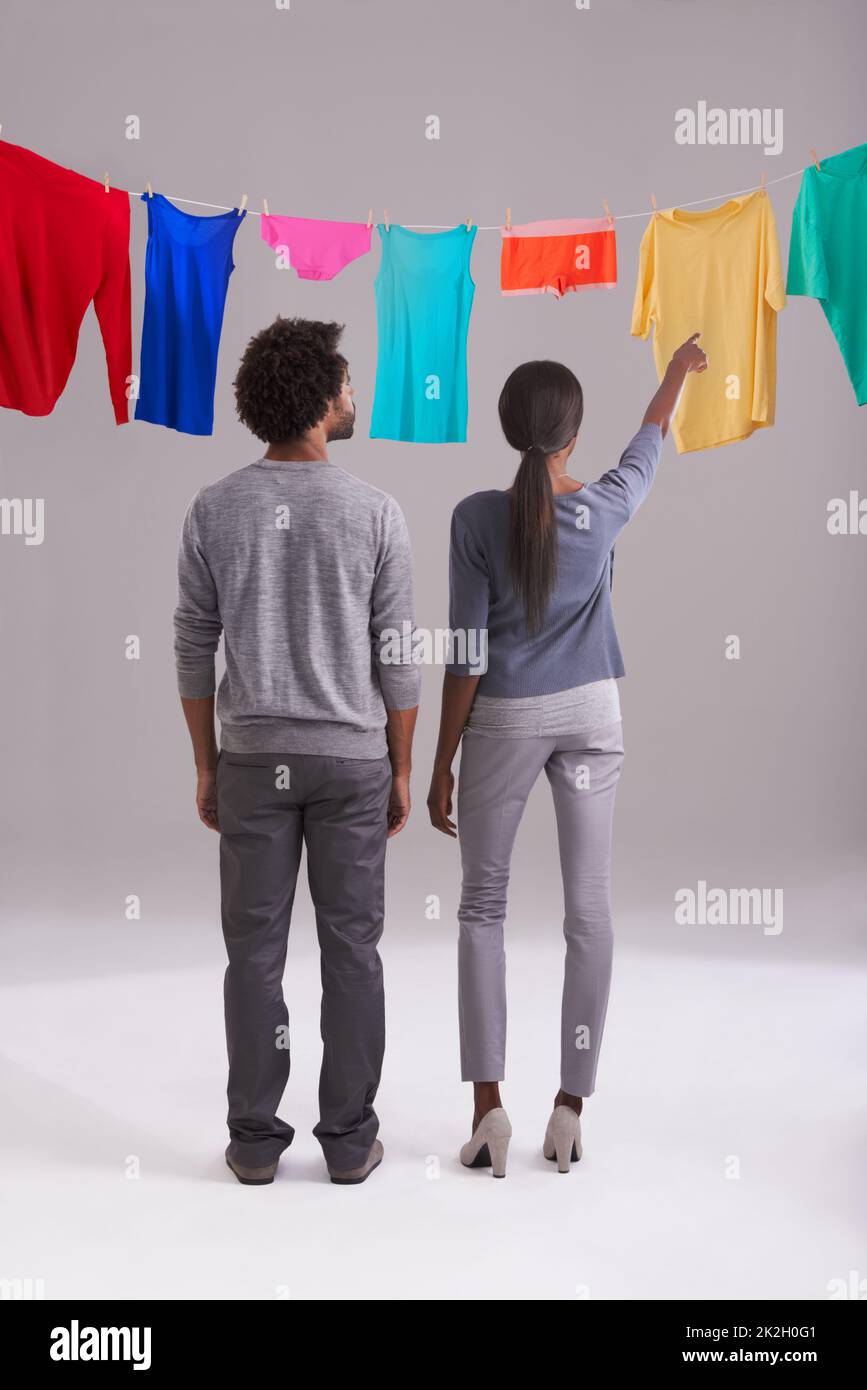 Und so hängen Sie die Wäsche auf. Studioaufnahme eines jungen Paares, das vor einer Wäscheleine voller farbenfroher Wäsche steht. Stockfoto