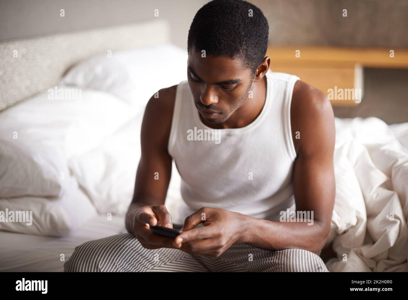 Mit Freunden verbunden, vom Komfort meines Bettes aus. Ein hübscher junger Mann, der im Bett saß und sein Handy benutzte. Stockfoto