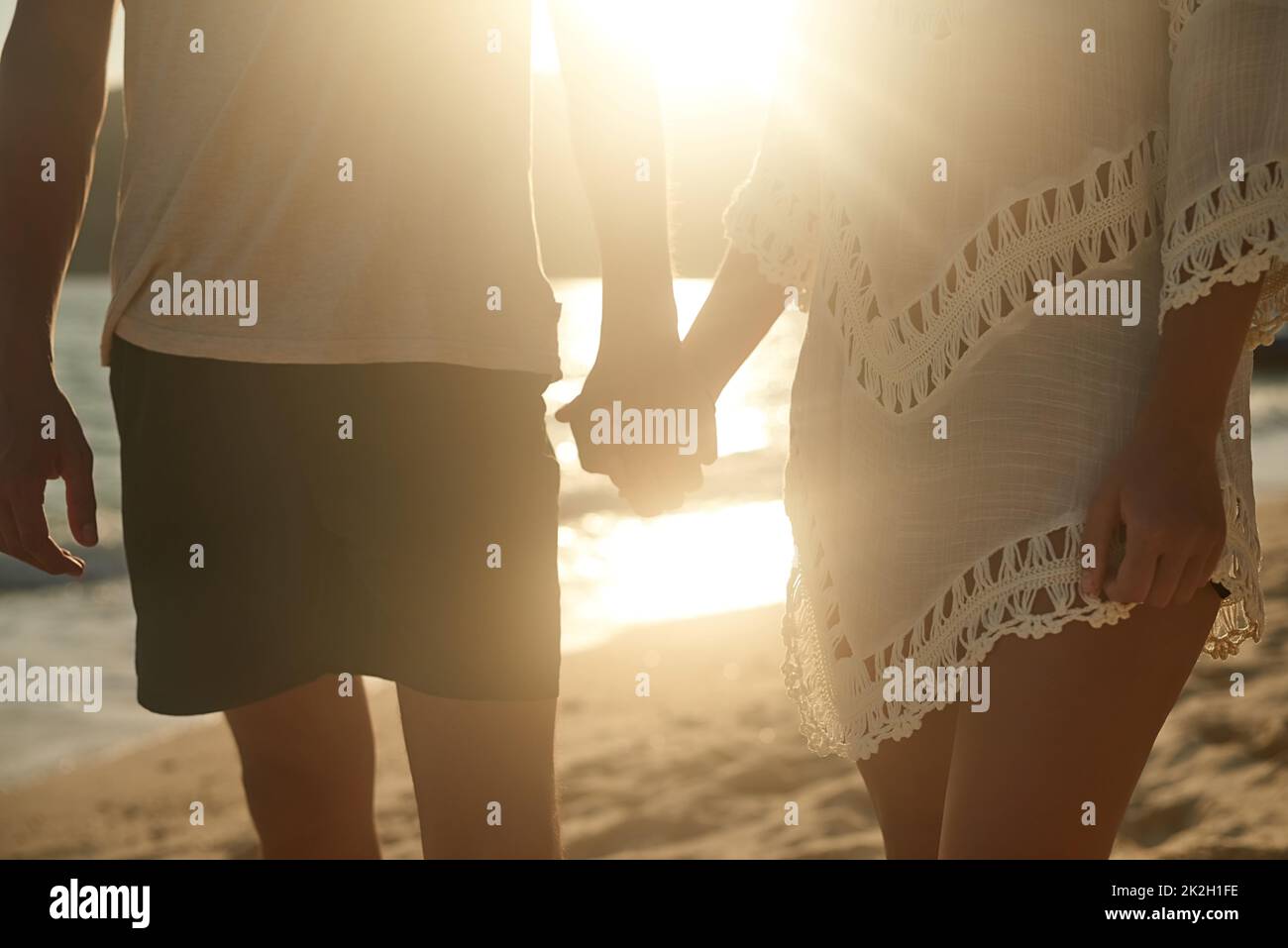 Hand in Hand auf dem Sand. Aufnahme eines liebevollen jungen Paares am Strand bei Sonnenuntergang. Stockfoto