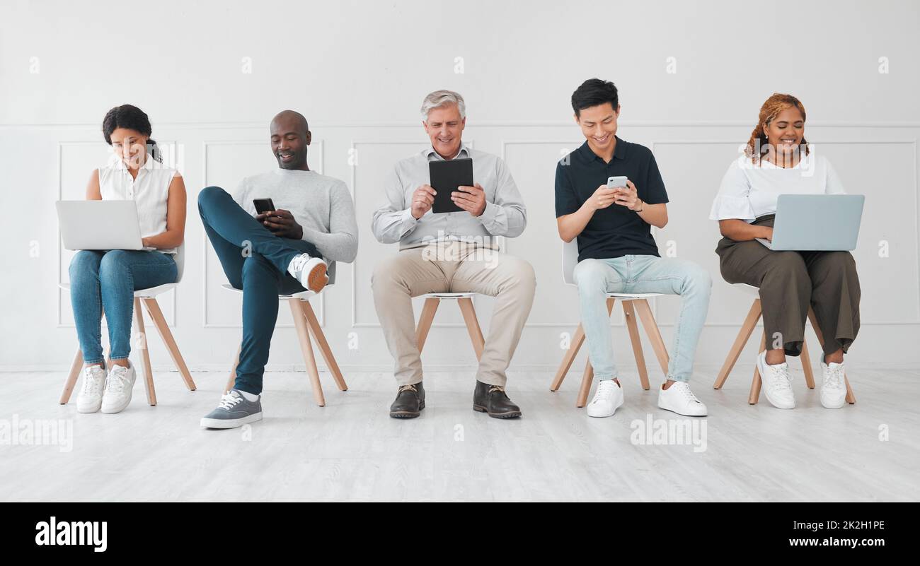 Ein paar lohnende Verbindungen herstellen, während sie warten. Aufnahme einer vielfältigen Gruppe von Menschen, die digitale Geräte nutzen, während sie vor weißem Hintergrund in der Schlange sitzen. Stockfoto