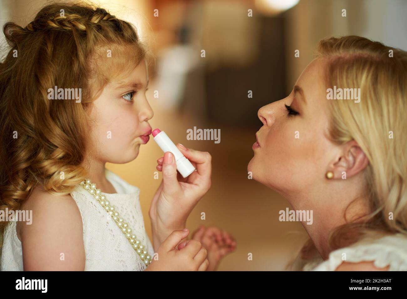 Verkleiden sich ihre kleine Prinzessin. Kurzer Schuss einer Mutter, die zu Hause Lippenstift auf ihre kleine Tochter anwendet. Stockfoto