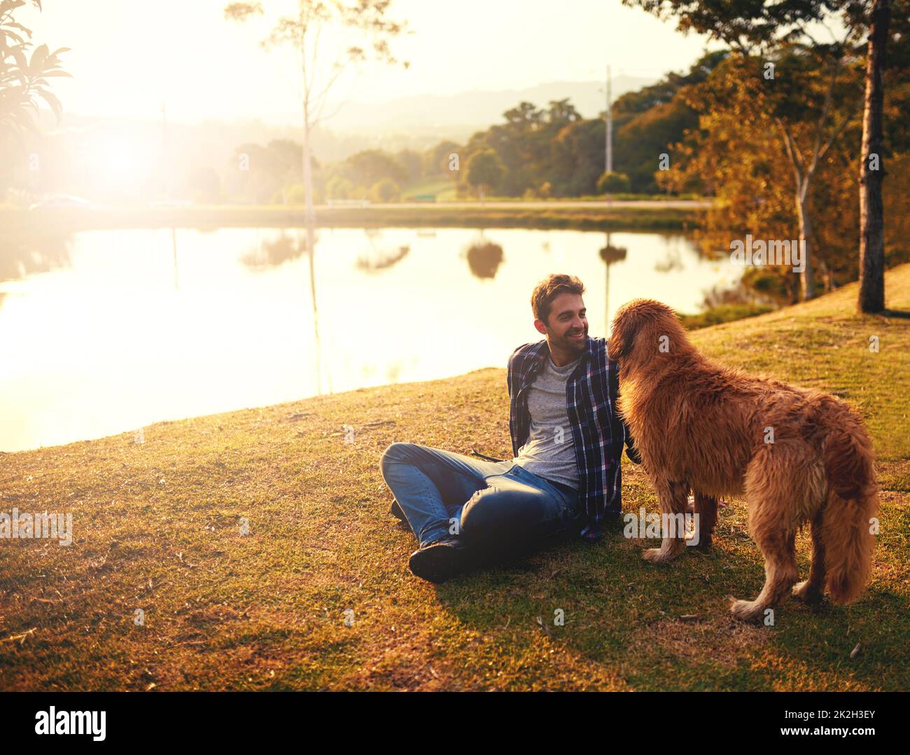 Sie haben Spaß. Ganzkörperaufnahme eines hübschen jungen Mannes und seines Hundes, der einen Tag an einem See im Park verbringt. Stockfoto