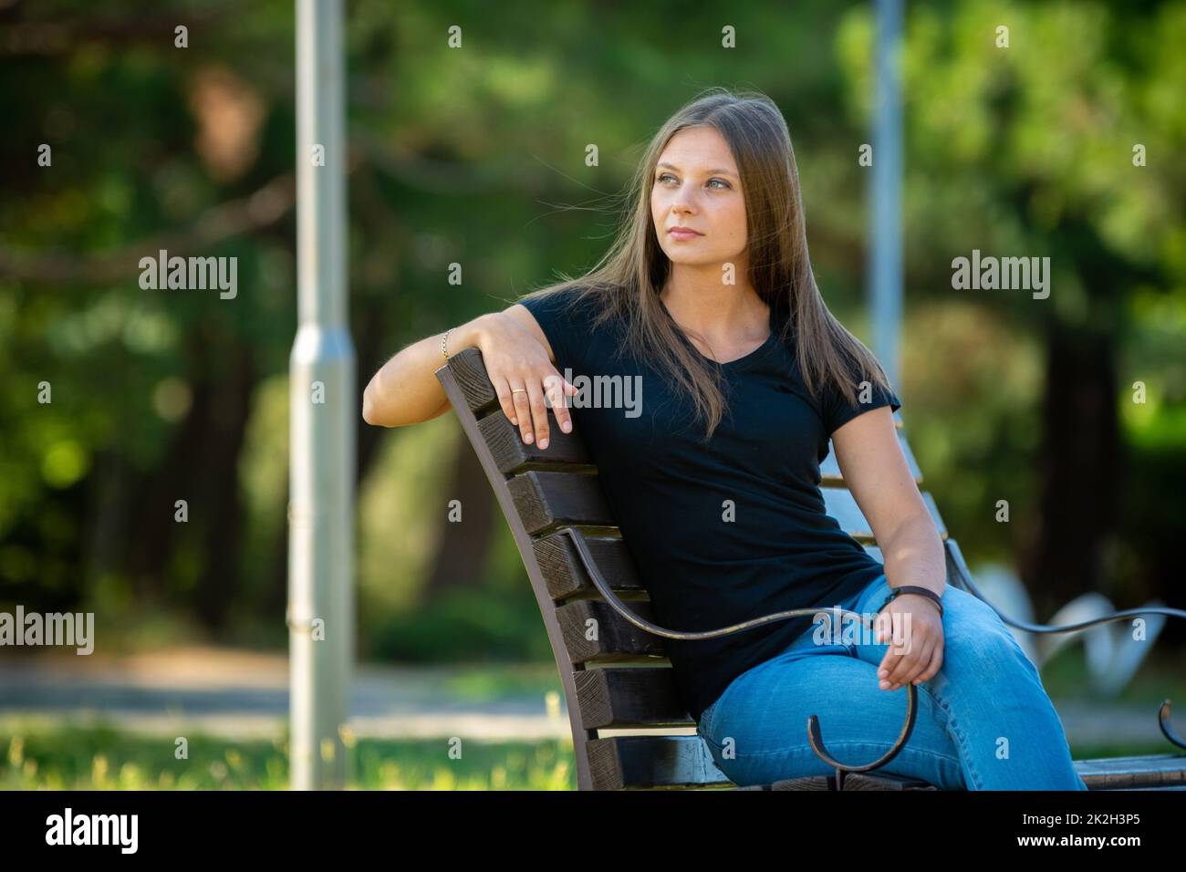 Ein schönes Mädchen in legerer Kleidung sitzt auf einer Bank in einem schönen grünen Park Stockfoto