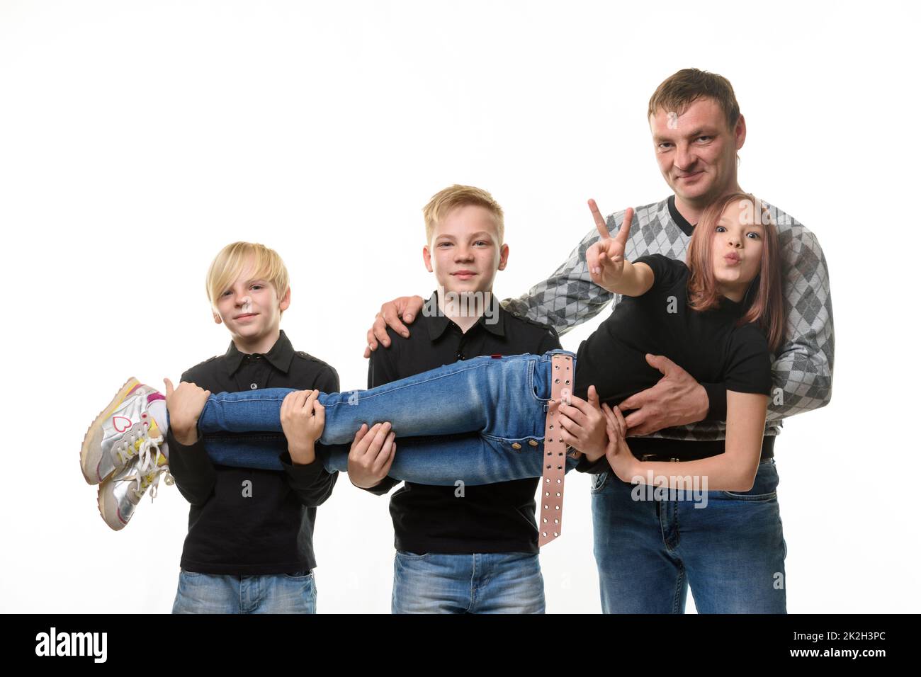 Vater und zwei Söhne halten ein Teenager-Mädchen in den Armen, Mädchen Freizeitkleidung in dunklen Farben, weißer Hintergrund Stockfoto