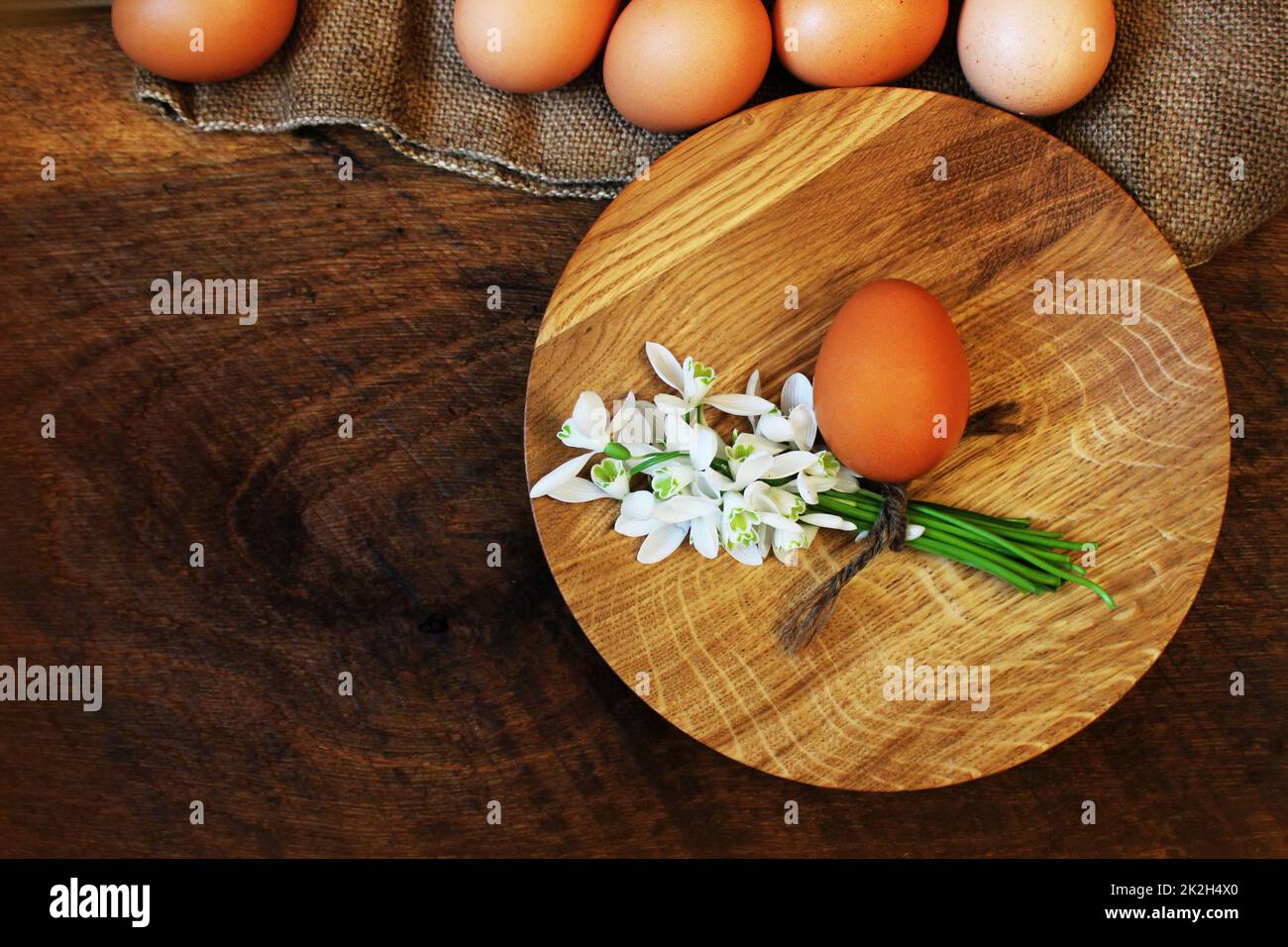 Ostern-Hintergrund. Rustikaler Holztisch mit Platte, Ei, Blumen und Schneidebrett. Ansicht von oben. Stockfoto