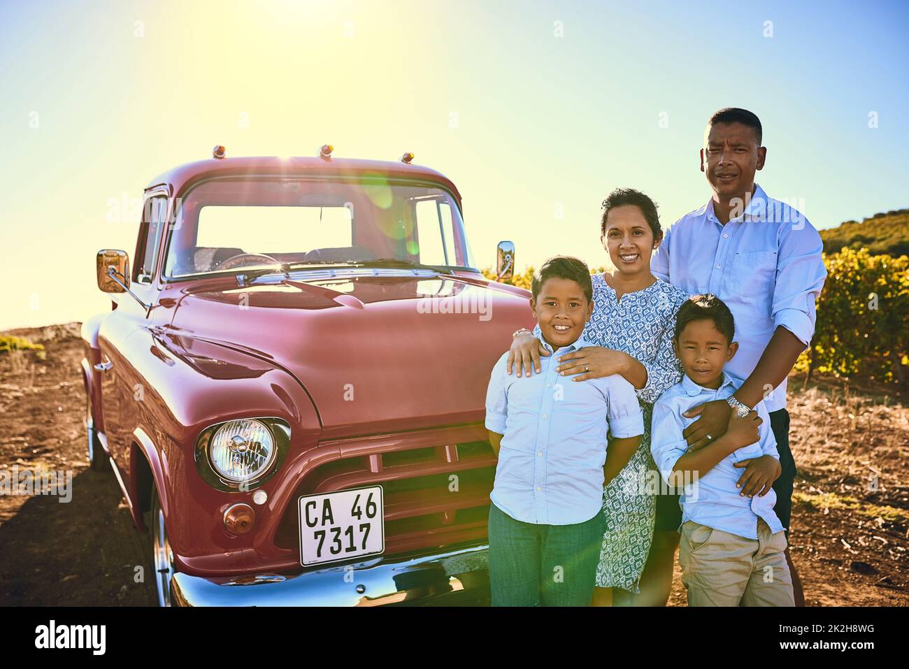 Die Familie und Familie Auto. Aufnahme einer fröhlichen Familie, die draußen neben einem roten Pickup-Truck für ein Porträt posiert. Stockfoto