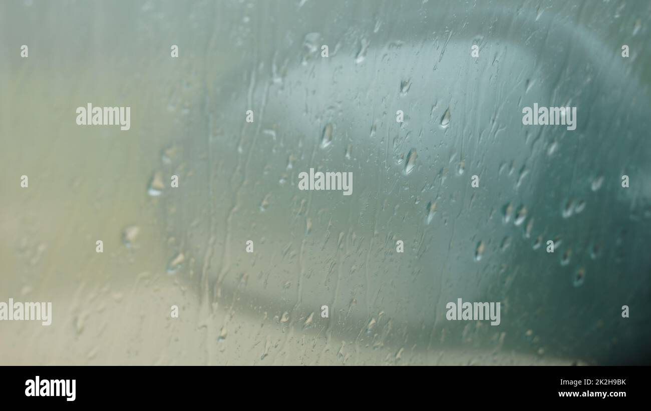 Verschwommener Regen fällt auf ein Autofenster mit dem Spiegel im Hintergrund. Nahaufnahme Stockfoto