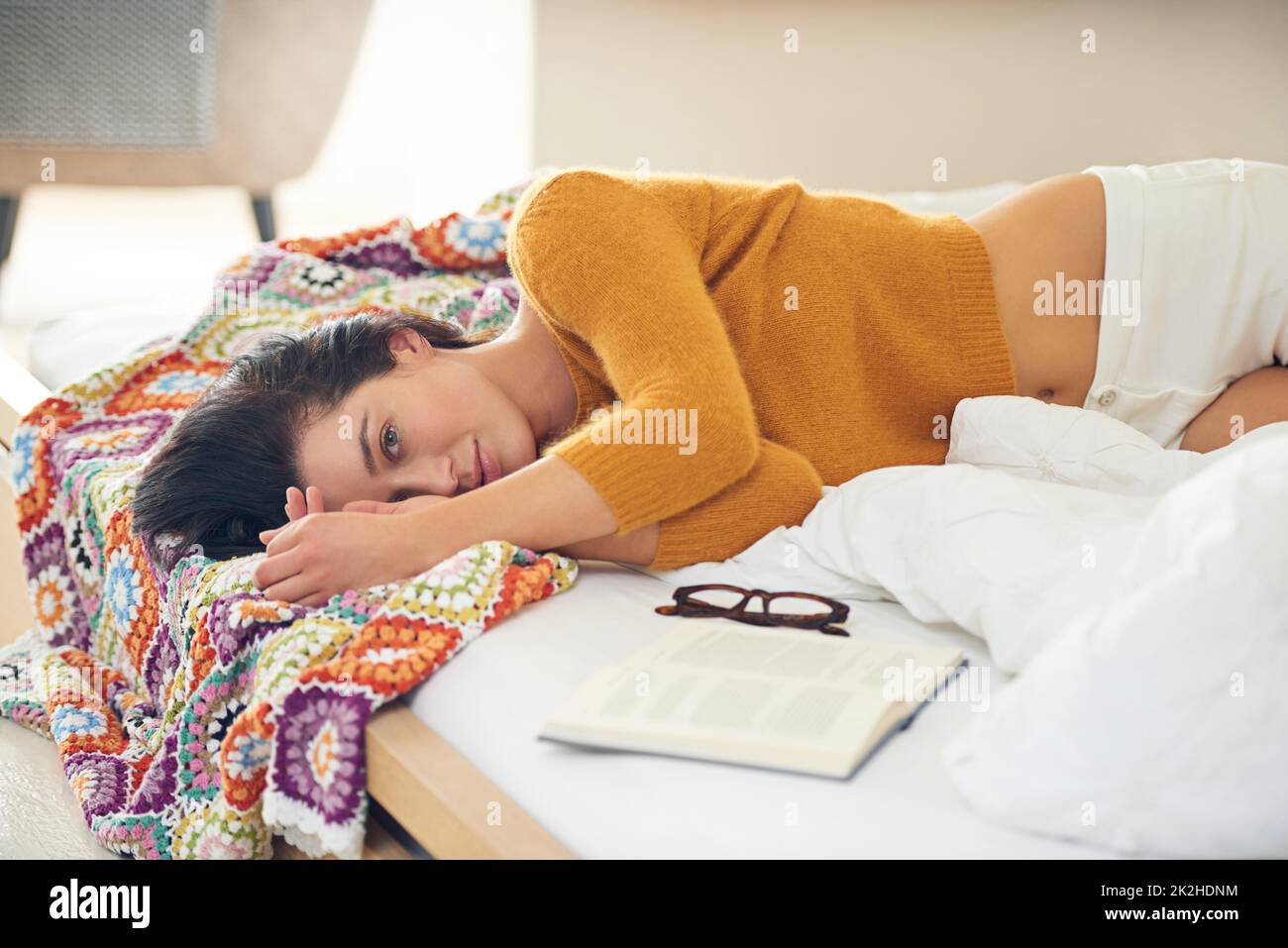 Eine Pause von einer guten Lektüre machen. Beschnittenes Porträt einer jungen Frau, die neben Lesematerial auf ihrem Bett liegt. Stockfoto