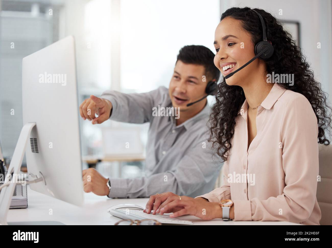 Austausch von Ratschlägen zur Verbesserung ihrer Dienste. Aufnahme von zwei Call Center-Agenten, die an einem Computer in einem Büro zusammenarbeiten. Stockfoto