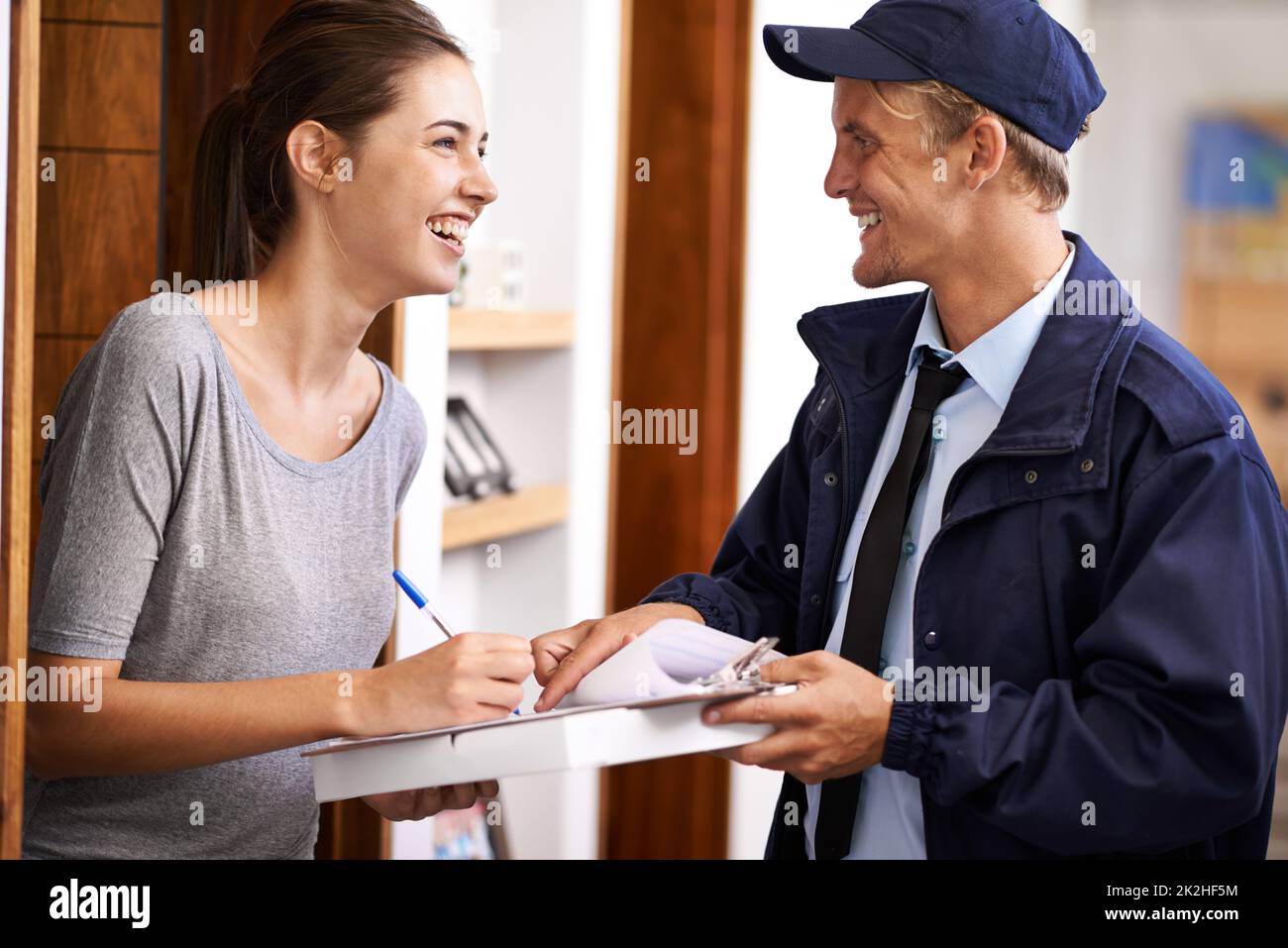 Es kommt immer pünktlich an. Ein Kurier, der eine Lieferung an einen lächelnden Kunden macht. Stockfoto