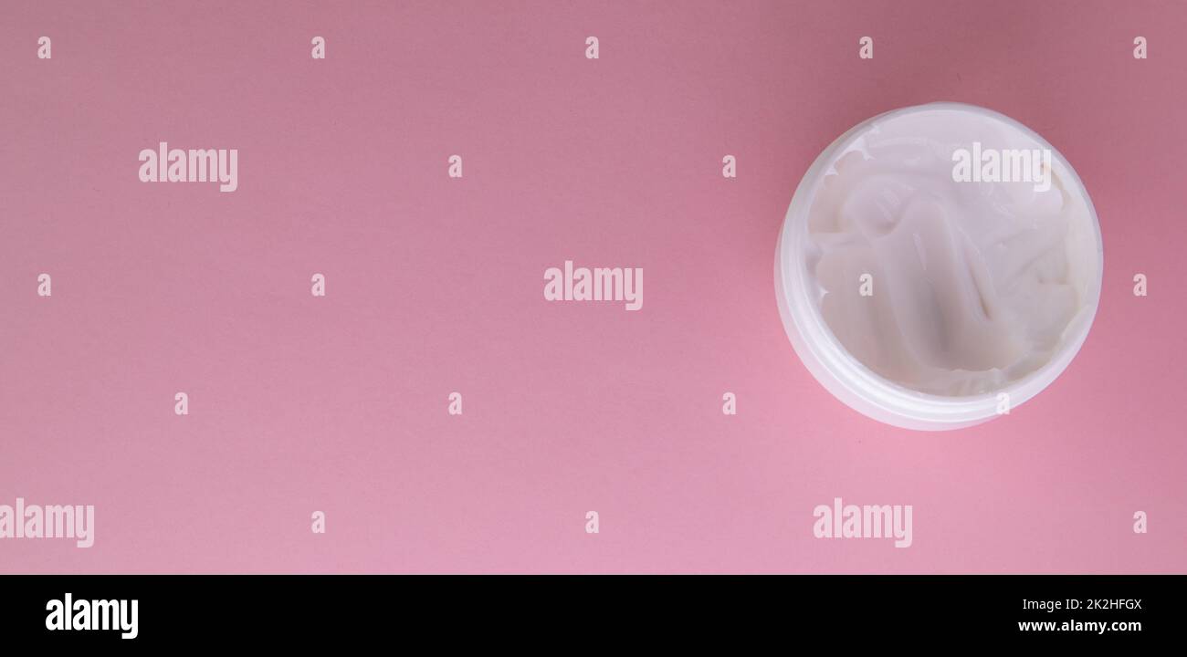 Weiße kosmetische Gesichtscreme in einem runden offenen Glas auf pinkfarbenem Hintergrund, Draufsicht, Kopie des Bereichs links Stockfoto