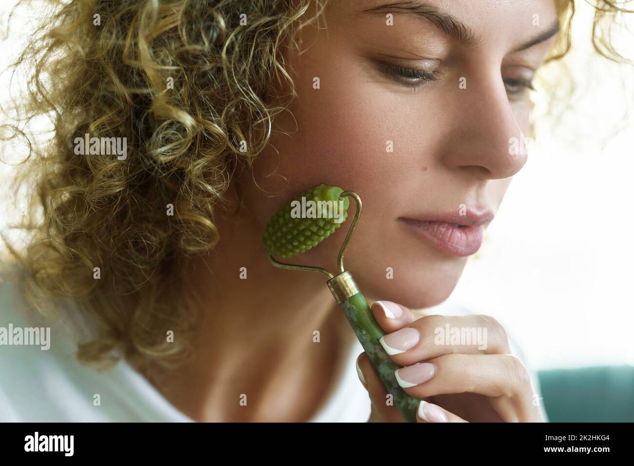 Schöne Frau, die zu Hause eine Gesichtsmassage mit einem Jade-Dermaroller macht Stockfoto