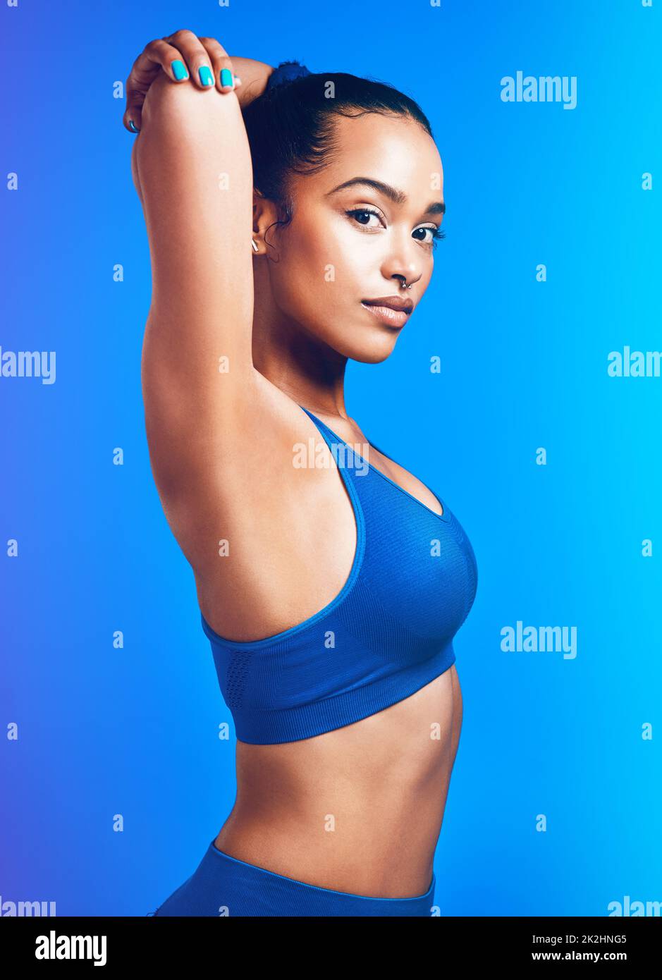 Fitness ist ein Lebensstil. Studioportrait einer attraktiven jungen Sportlerin, die ihre Arme vor blauem Hintergrund streckt. Stockfoto