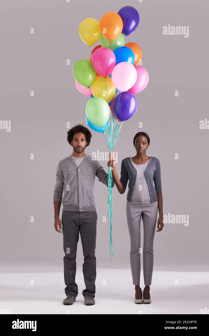 Verleihen Sie Ihrem Leben Farbe. Studioaufnahme eines jungen Paares, das einen Haufen Ballons zusammenhält. Stockfoto