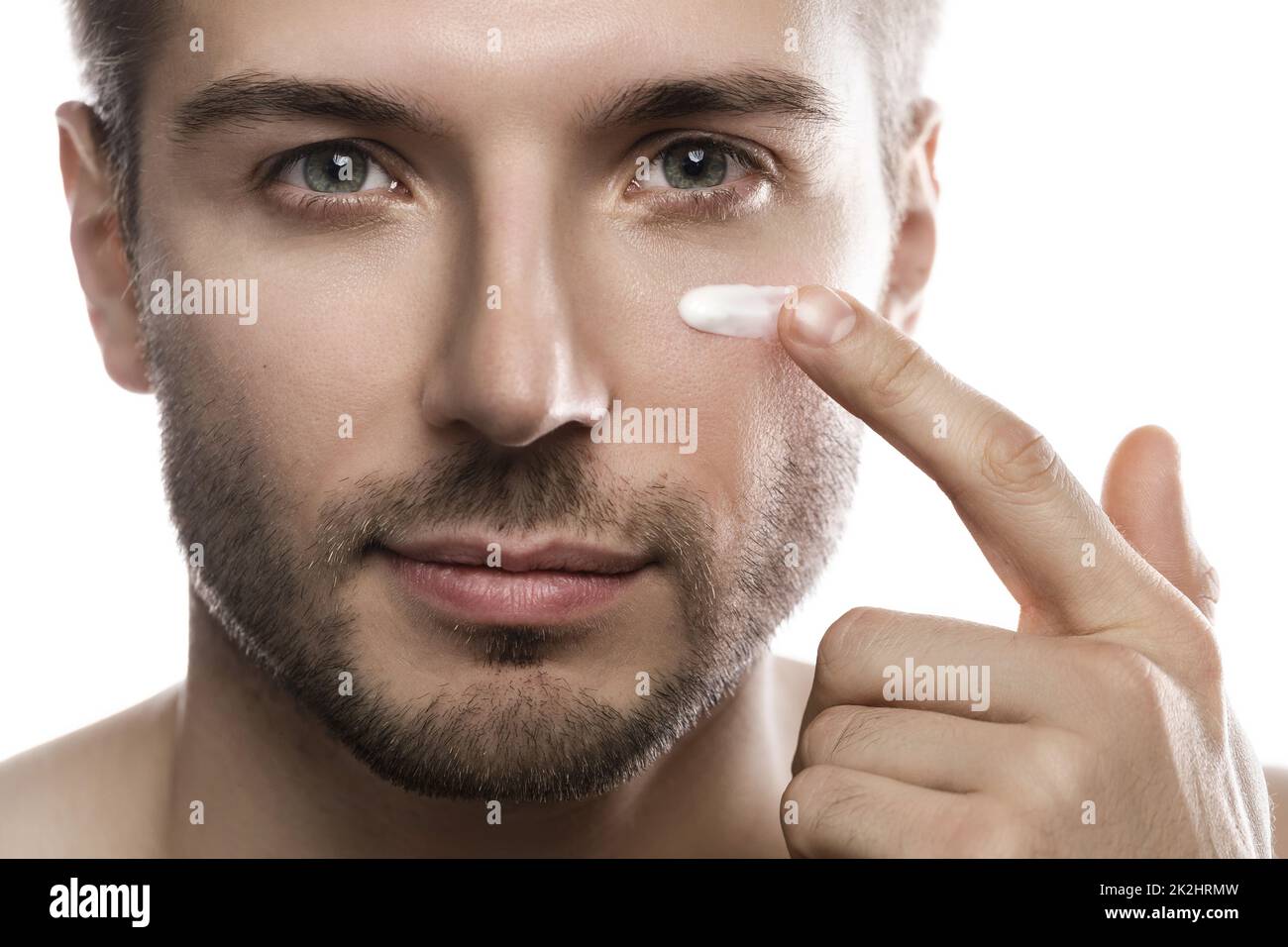 Schönheit für Männer. Der junge Mann wendet feuchtigkeitsspendende und Anti-Aging-Creme auf sein Gesicht an Stockfoto