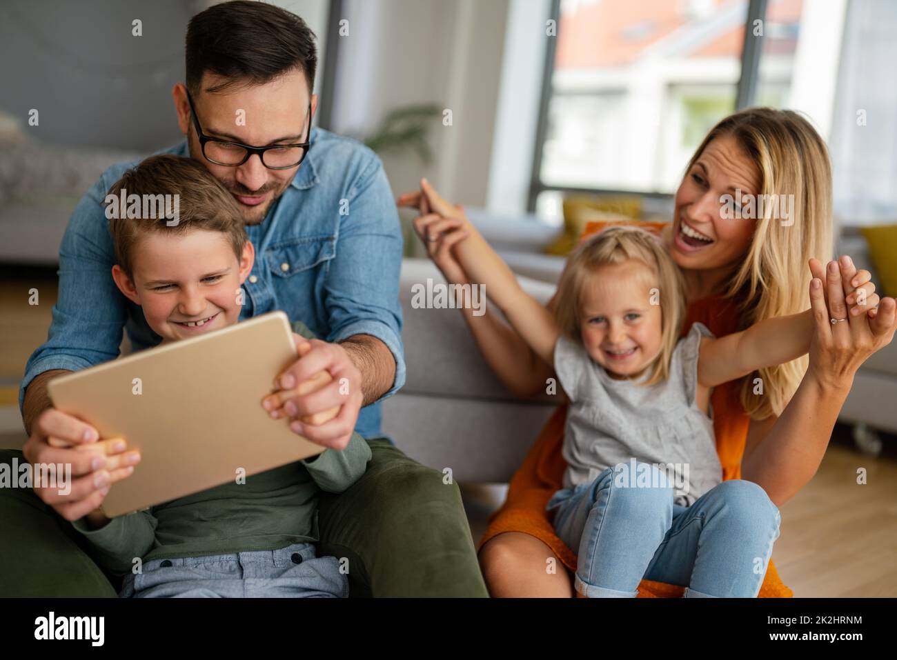 Glückliche junge Familie, die Spaß zu Hause hat. Eltern mit Kindern, die ein digitales Gerät verwenden. Stockfoto