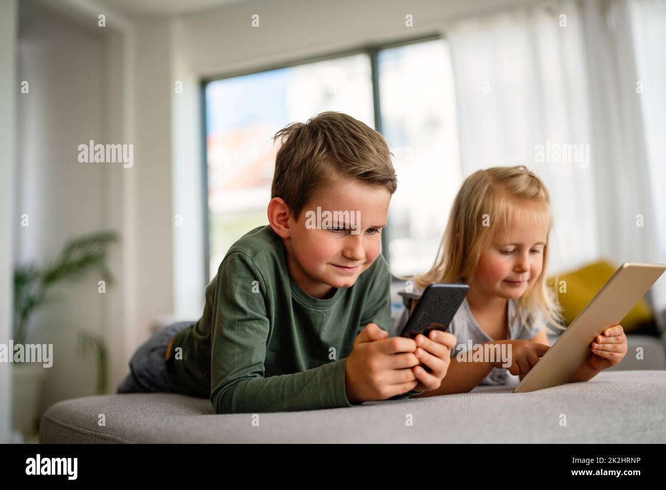 Kleine Mädchen und Jungen, die Videos anschauen oder Spiele auf ihrem digitalen Gerät Tablet, Smartphone spielen. Stockfoto