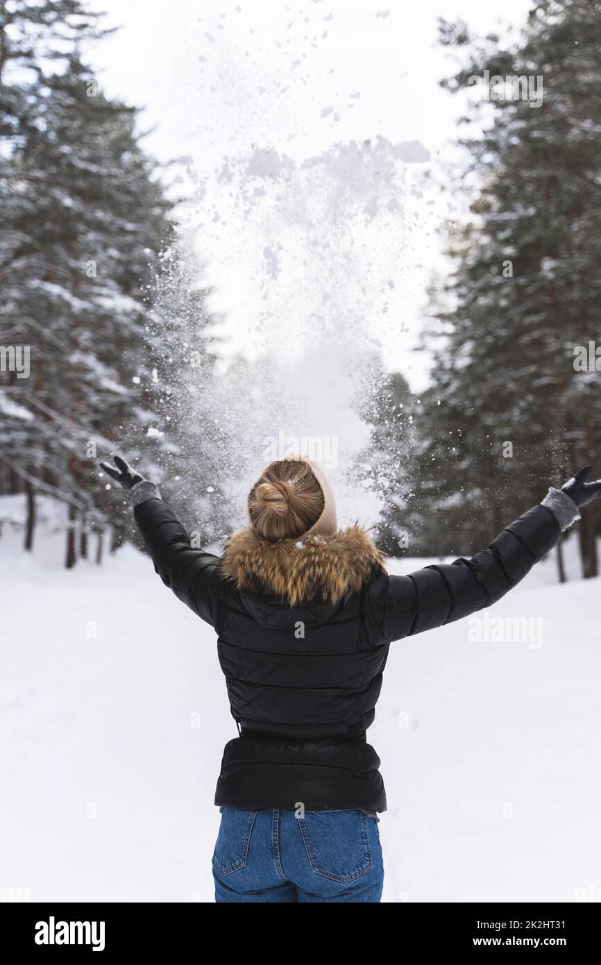 Frau, die während des kalten Wintertages Schnee in die Luft wirft Stockfoto