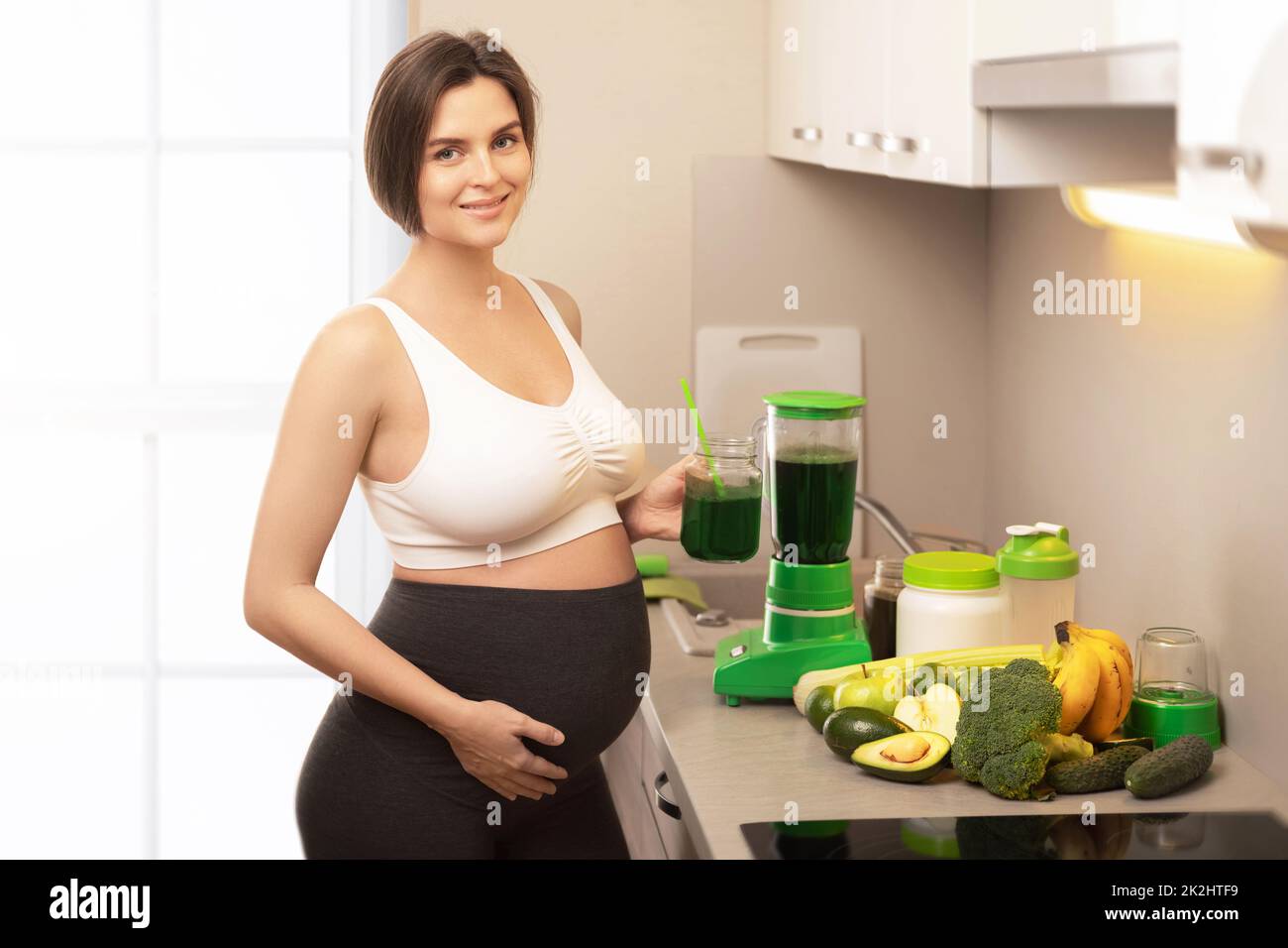 Glückliche schwangere Frau, die einen gesunden grünen Smoothie trinkt Stockfoto