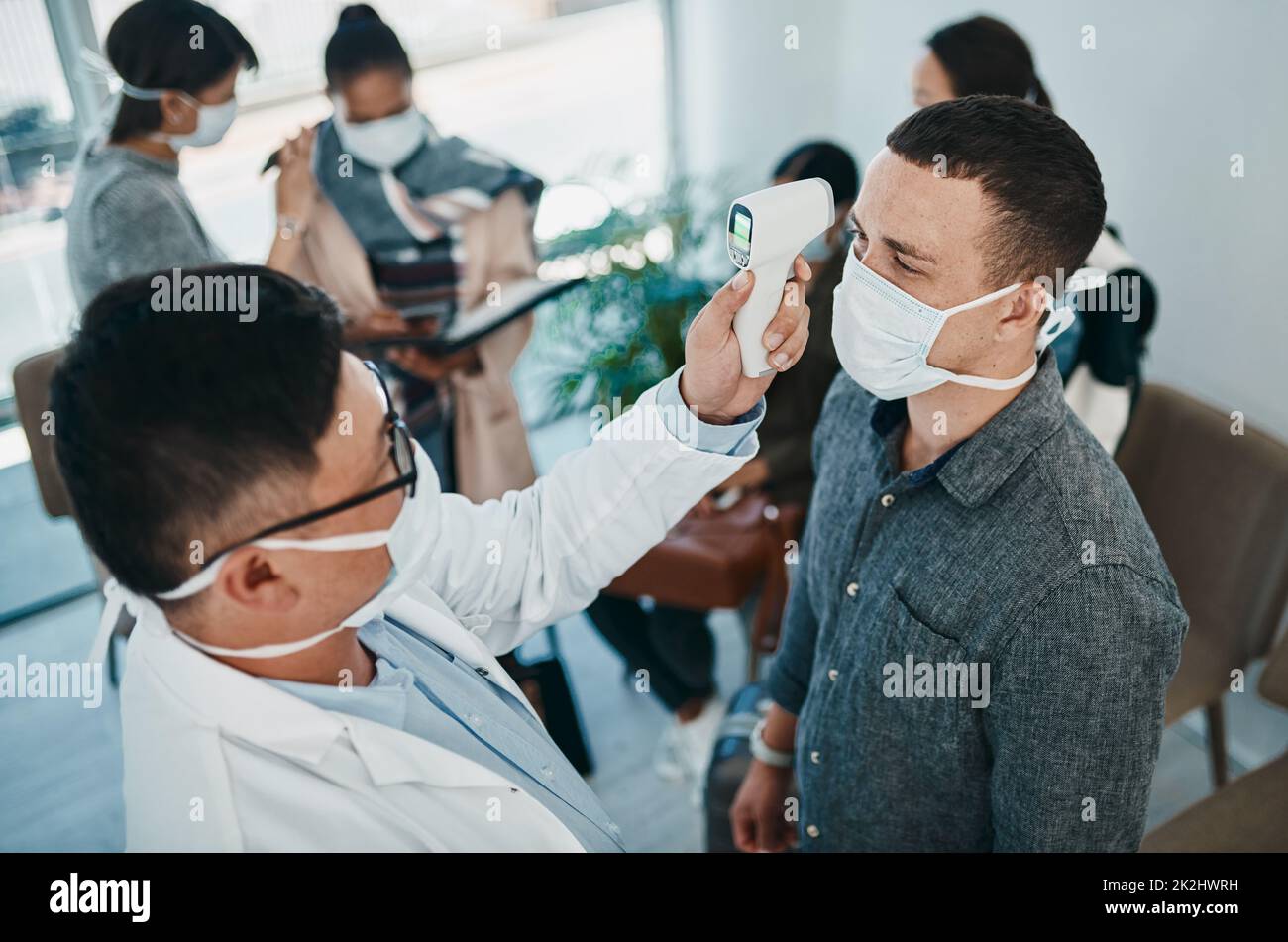 Es beginnt alles mit Fieber. Aufnahme eines jungen Mannes, der während eines Ausbruchs mit einem Infrarotthermometer von einem Mitarbeiter des Gesundheitswesens die Temperatur erfasst hat. Stockfoto