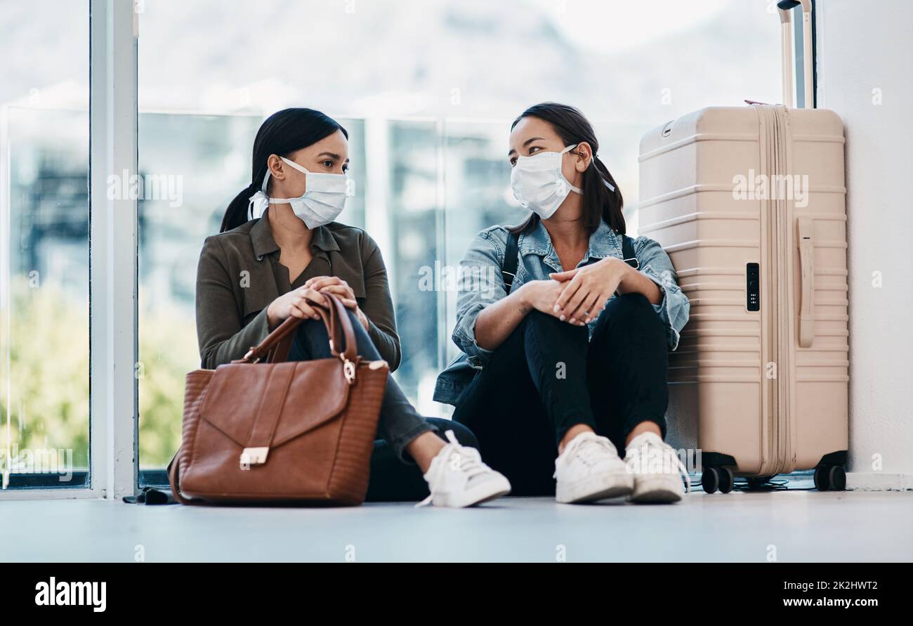 Es dauerte eine Distanz, um uns zu verbinden. Aufnahme von zwei jungen Frauen, die Masken tragen, während sie gemeinsam auf einem Flughafen warten. Stockfoto