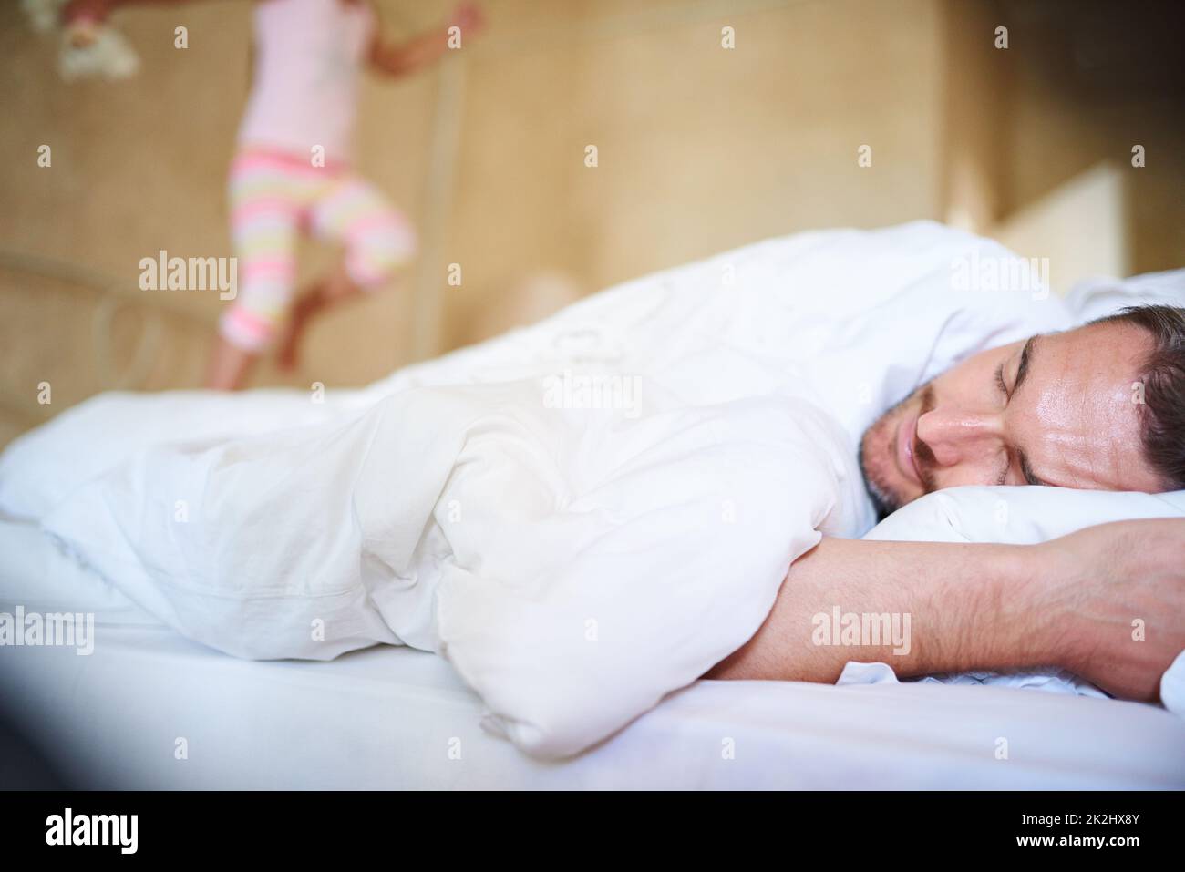 Es ist Morgen, Dvory. Aufnahme eines schlafenden Vaters mit seiner kleinen Tochter, die auf das Ende des Bettes springt. Stockfoto