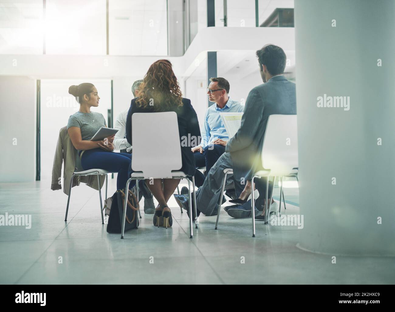 Die Details aufknöpfen. Aufnahme einer Gruppe von Kollegen, die miteinander reden, während sie im Kreis in einem Büro sitzen. Stockfoto