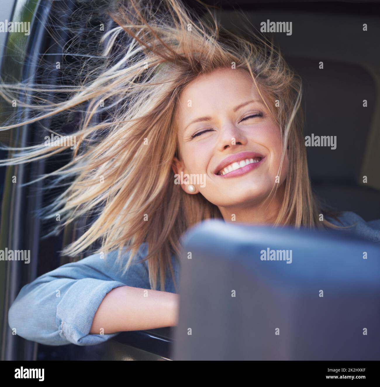 Spüren Sie den Wind in Ihren Haaren Eine junge Frau spürt die Brise in ihren Haaren durch ein offenes Autofenster. Stockfoto