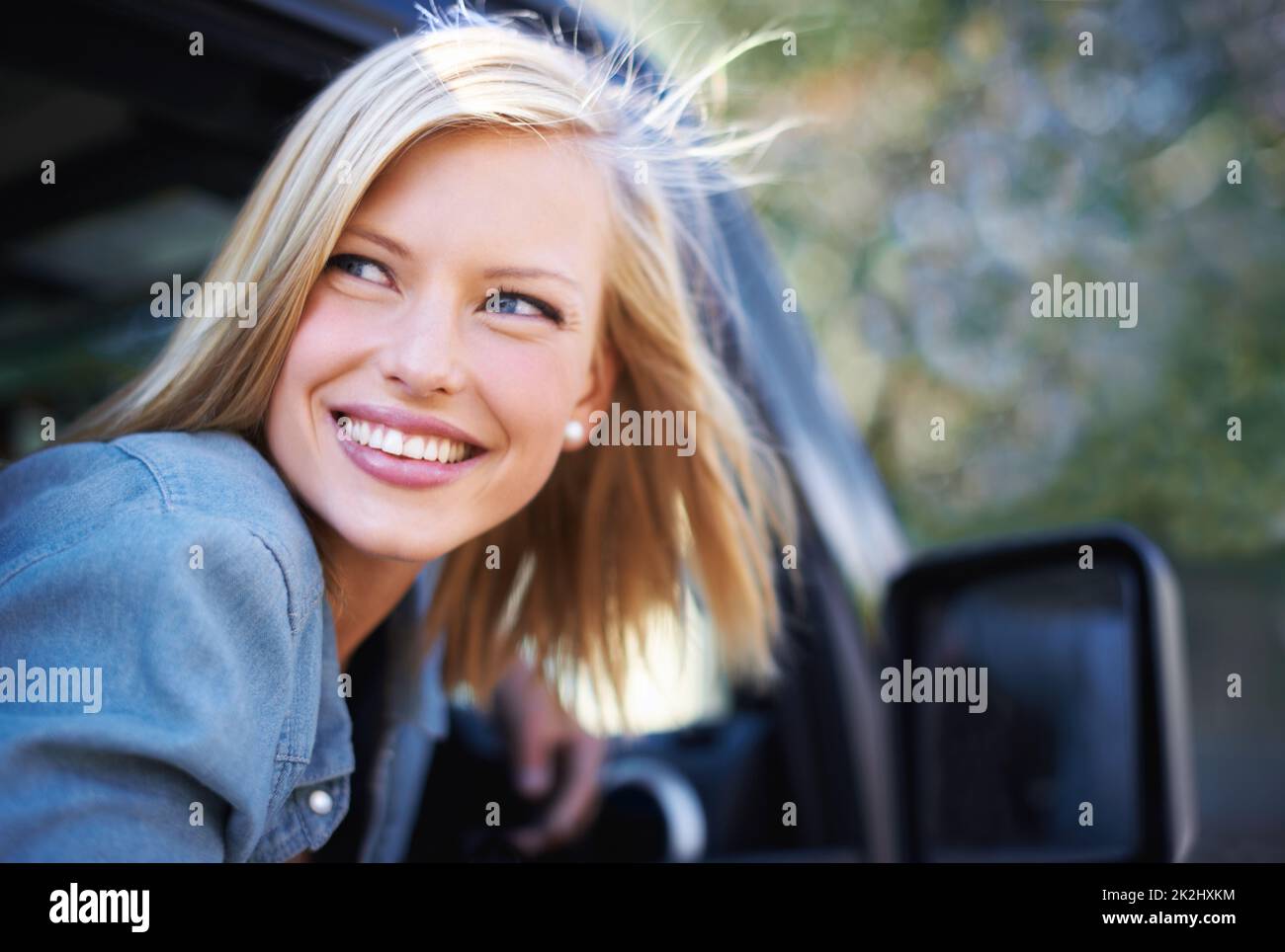 Sich im Freien sorglos fühlen. Eine junge Frau spürt die Brise in ihren Haaren durch ein offenes Autofenster. Stockfoto