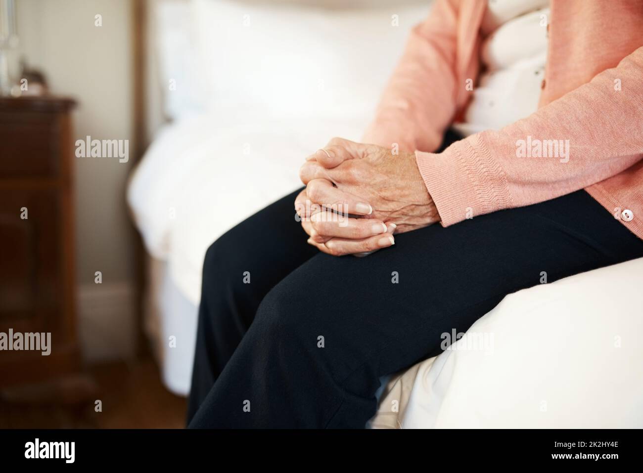 Worauf warte ich noch? Ausgeschnittene Aufnahme einer älteren Frau, die in einem Pflegeheim am Rand eines Bettes sitzt. Stockfoto
