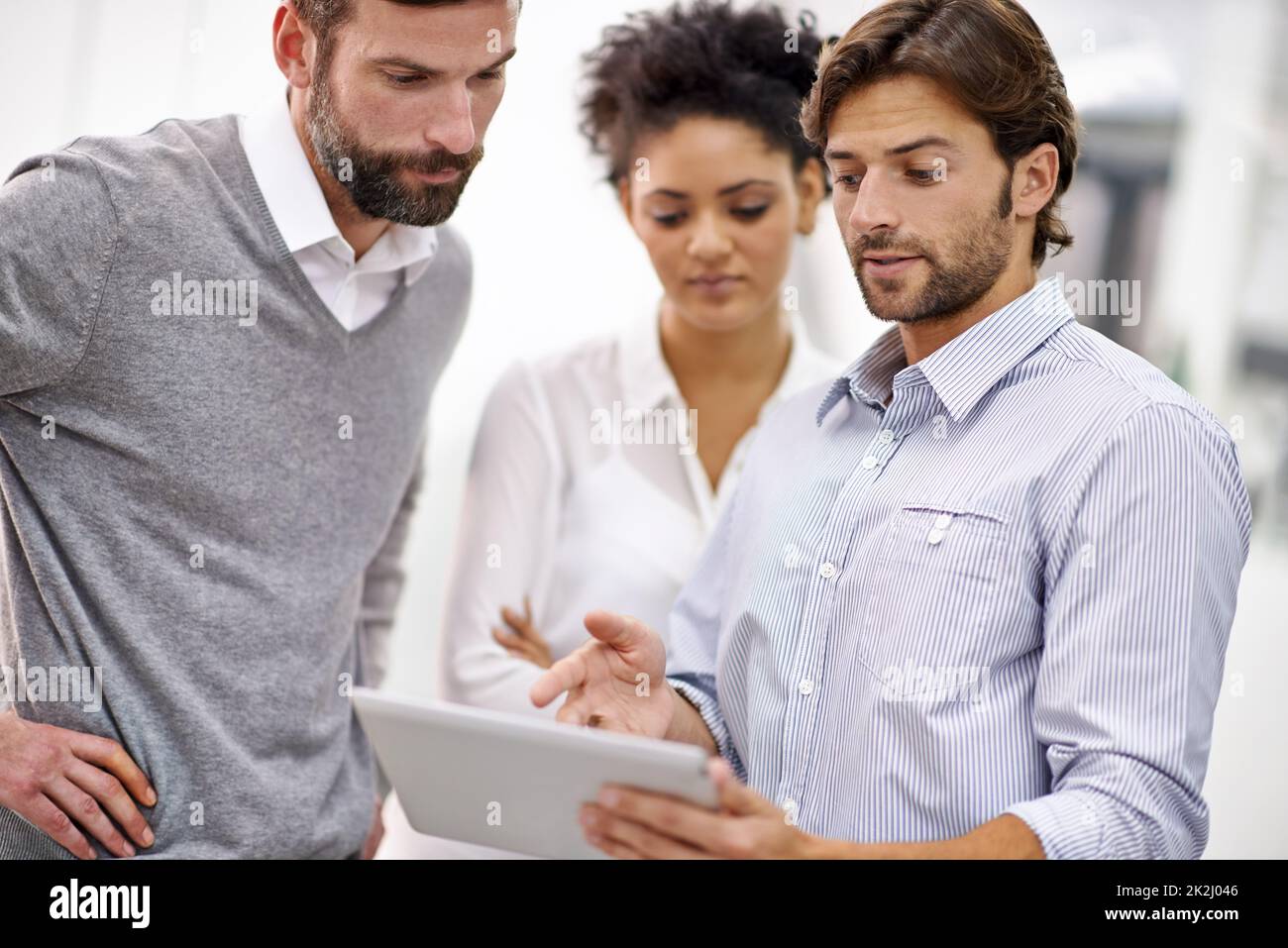 Gehen Sie über die Projekte Online-Präsenz. Aufnahme von drei jungen Geschäftsleuten, die in seinem Büro stehen und über ein Tablet reden. Stockfoto