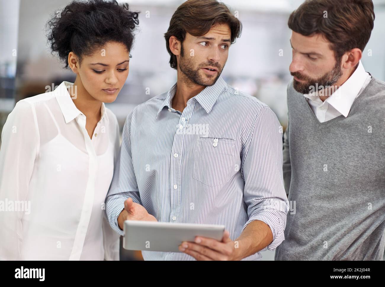 Gehen Sie über die Projekte Online-Präsenz. Aufnahme von drei jungen Geschäftsleuten, die in seinem Büro stehen und über ein Tablet reden. Stockfoto
