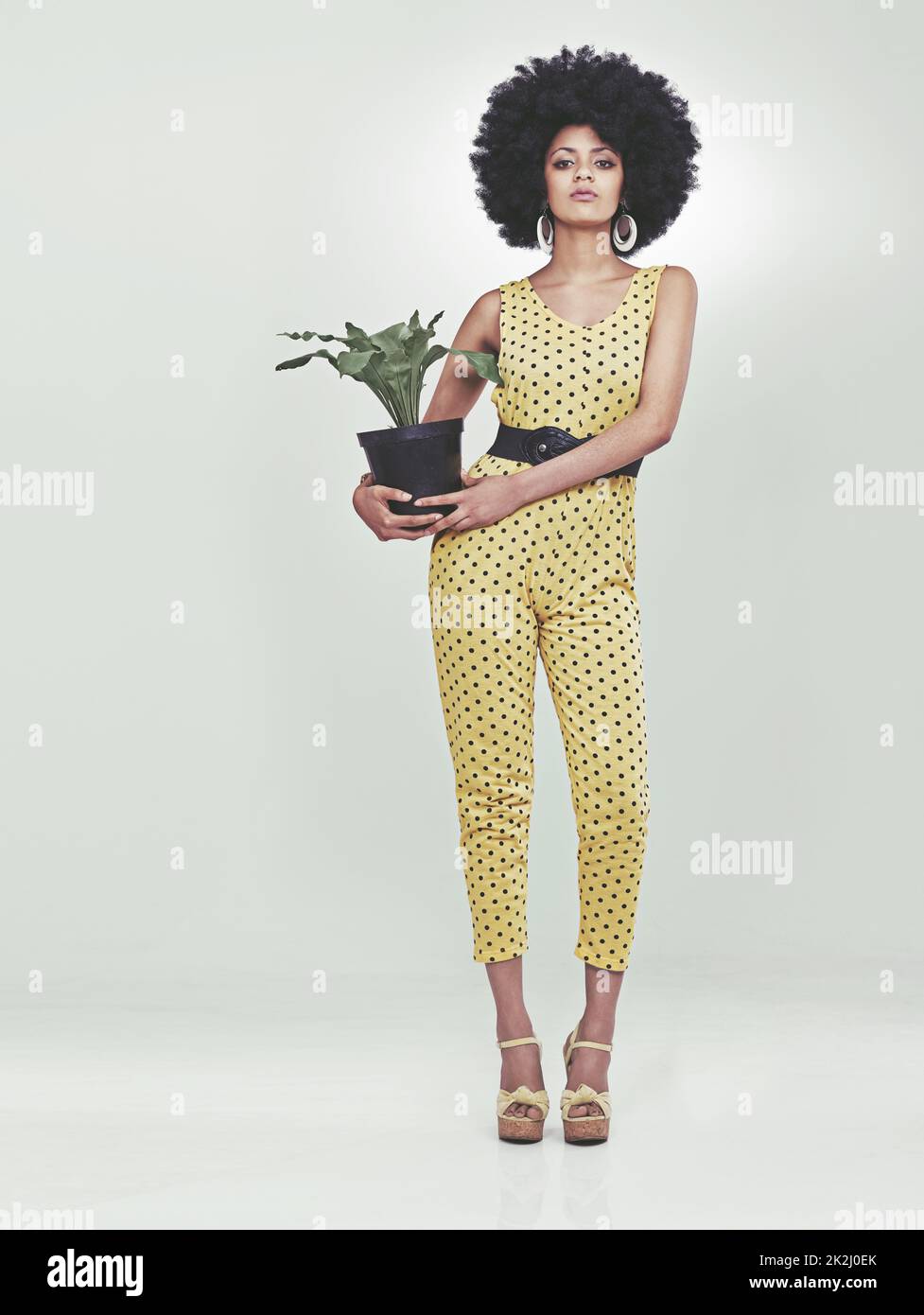 Sie hat Stil... und eine Pflanze... In voller Länge Porträt einer jungen Frau, die einen 70s Retro-Jumpsuit mit einer Topfpflanze trägt. Stockfoto