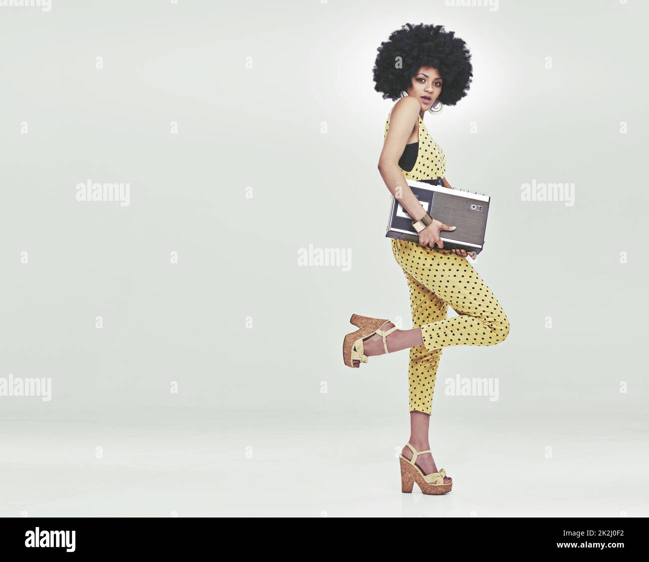 Zeit zur Disco. Eine junge Frau, die einen Retro-Jumpsuit aus dem Jahr 70s trägt, einen Kassettenspieler hält und eine Disco-Pose aufwirft. Stockfoto