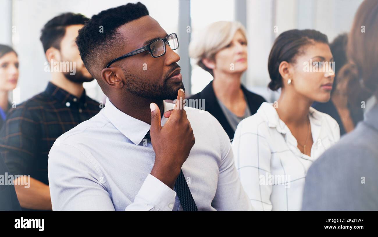 Hmm, so viel zu denken. Eine kleine Aufnahme eines hübschen jungen Geschäftsmanns, der tagsüber mit seinen Kollegen im Büro sitzt. Stockfoto