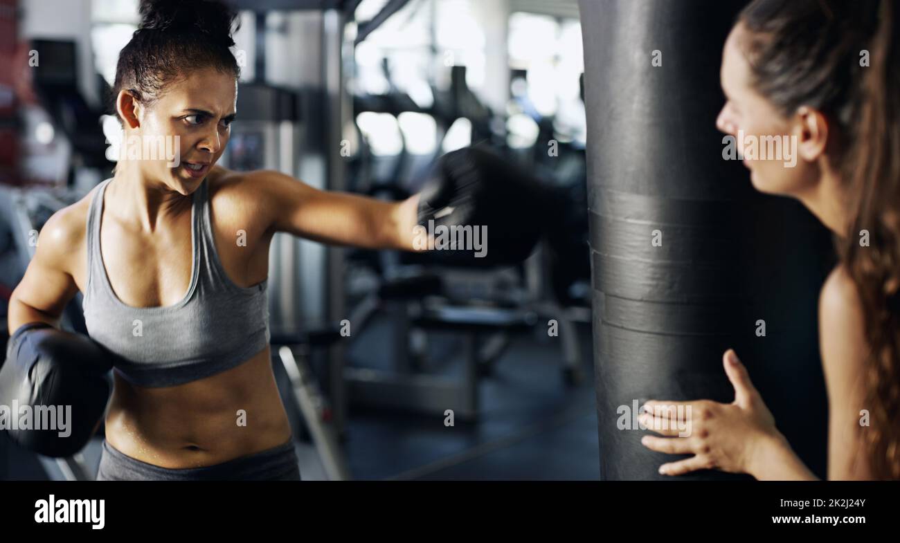 Achten Sie auf Ihr Formular. Eine kurze Aufnahme einer jungen Boxerin, die mit ihrem Trainer im Fitnessstudio an einem Boxsack trainiert. Stockfoto